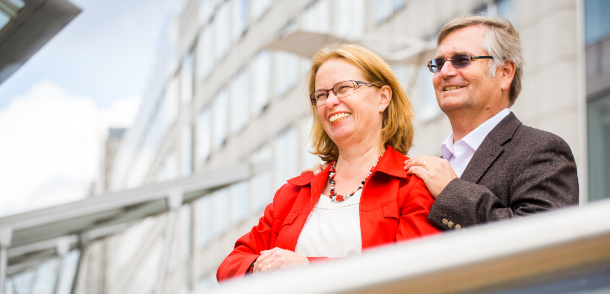 Man and woman standing with their arms around each other, looking off into the distance