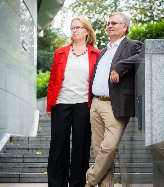 Man and woman standing beside each other, leaning against a wall and looking off into the distance