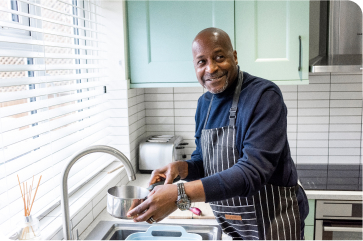 Smiling man wearing an apron and washing dishes.