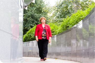 Smiling woman walking along paved path beside large decorative planters.