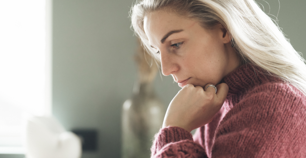 Young girl with her hand under her chin looks down at something on a table in front of her.