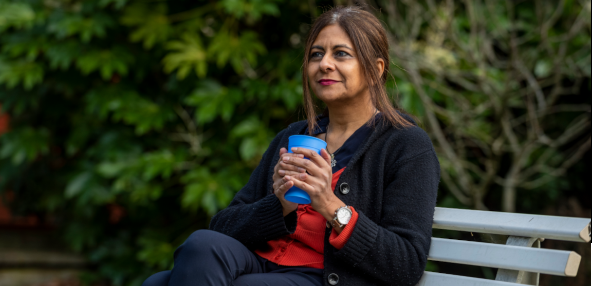 Lady sitting on bench, smiling and holding a blue cup